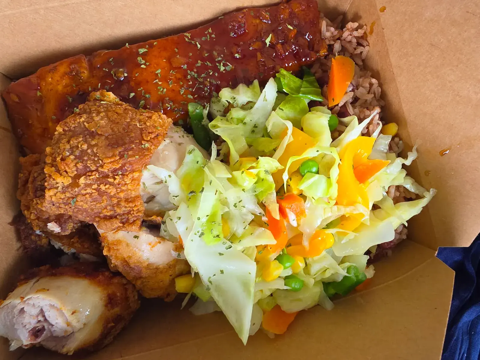 A boxed meal of fried chicken, rice and peas and steamed cabbage