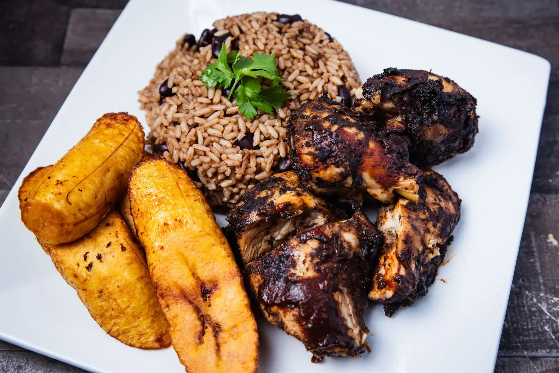 Jerk chicken with rice and peas and fried sweet plantain on a white plate